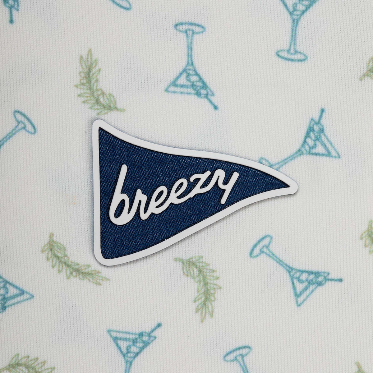 Patch with 'breezy' text on a fabric background with cocktail patterns