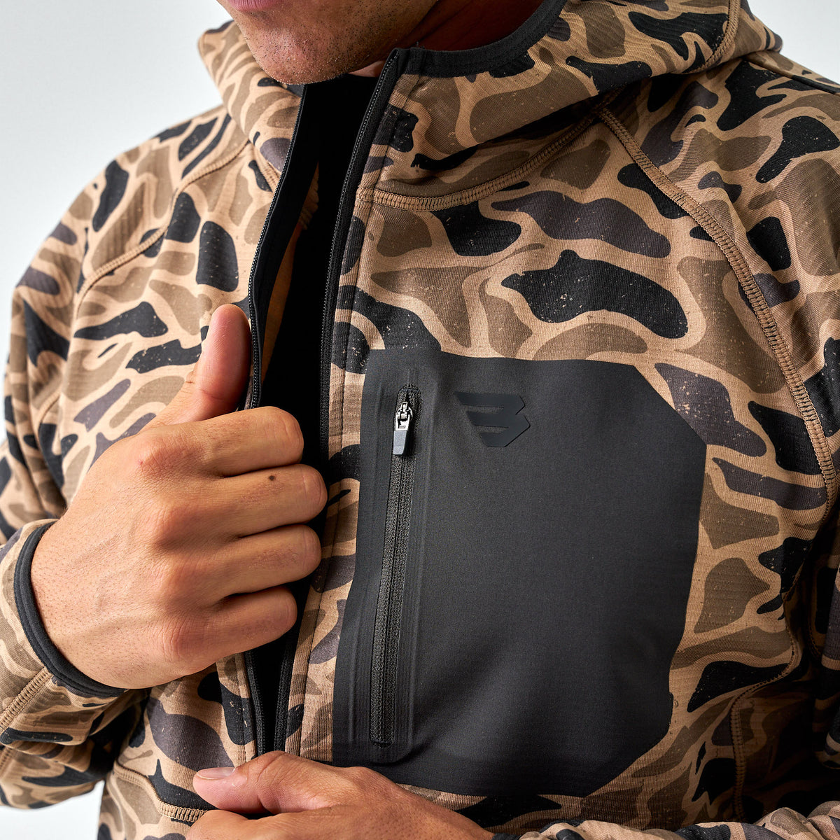Men’s camo quarter-zip hoodie in brown and black pattern with a solid black chest pocket, shown partially zipped.