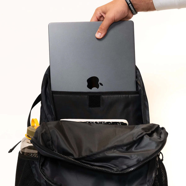 Person placing a laptop into a black backpack with a white background