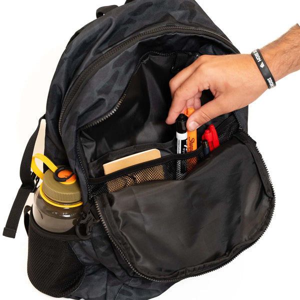 Black backpack with a hand reaching in to organize items on a white background