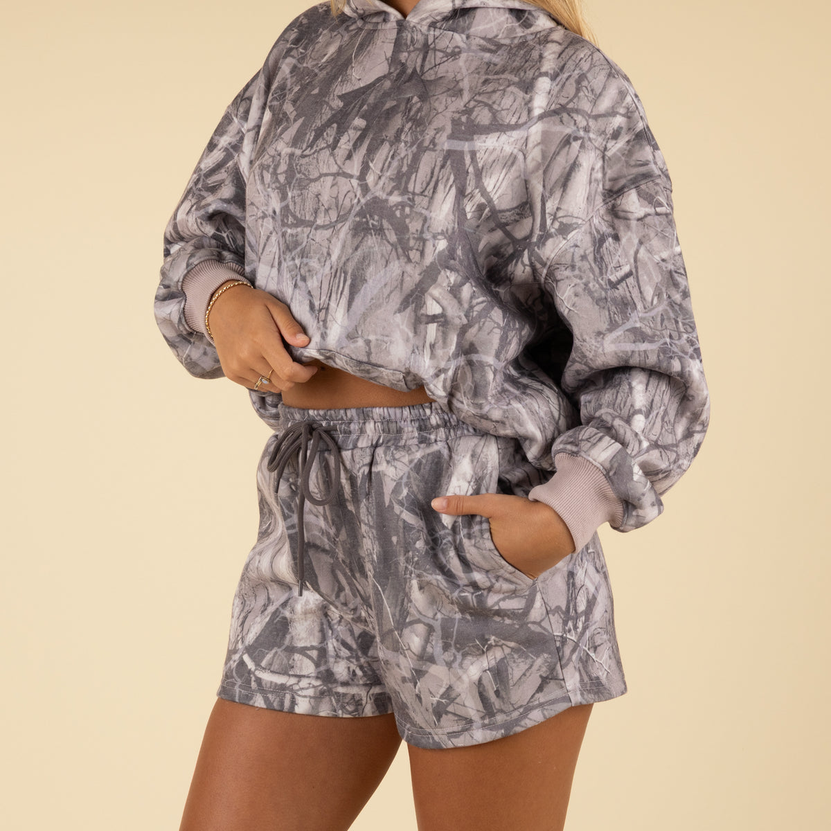 Person wearing a gray camouflage hoodie and shorts set on a beige background