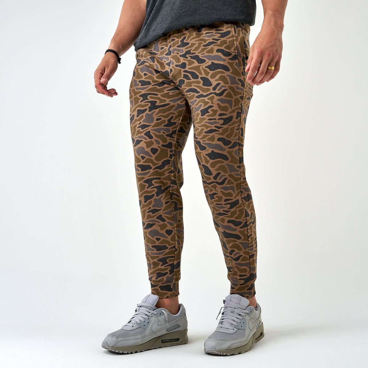 Front view of men’s camo jogger pants paired with a dark gray tee and gray sneakers, styled with tapered ankle cuffs.