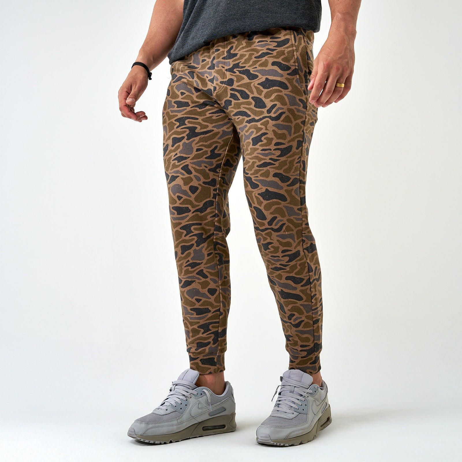 Front view of men’s camo jogger pants paired with a dark gray tee and gray sneakers, styled with tapered ankle cuffs.