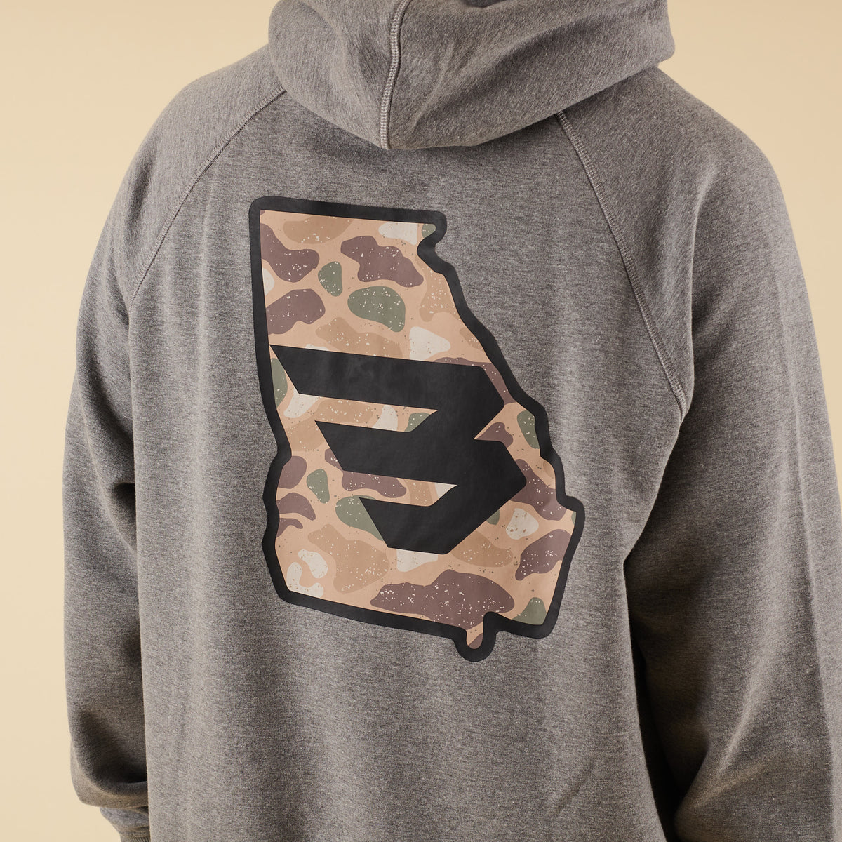 Close-up of the back of a gray hoodie featuring a large camo-pattern logo graphic centered between the shoulders.