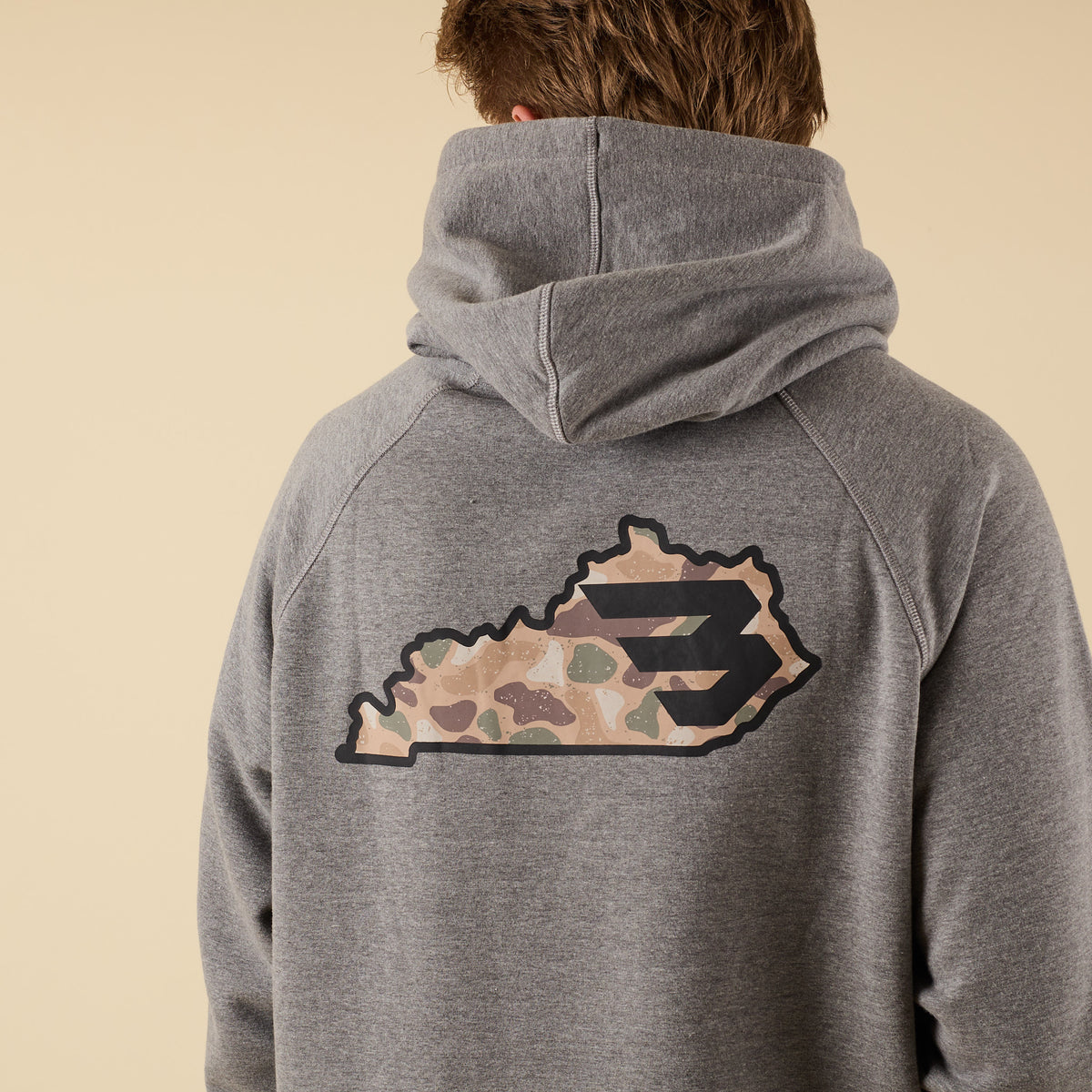 Back view of a gray hoodie with a large camo-pattern logo graphic centered between the shoulders.