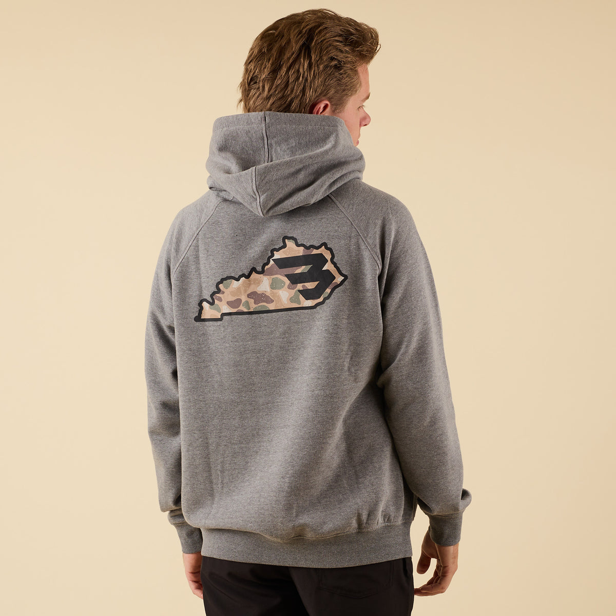 Man wearing a dark heather grey Burlebo hoodie with a camo filled Kentucky state design.