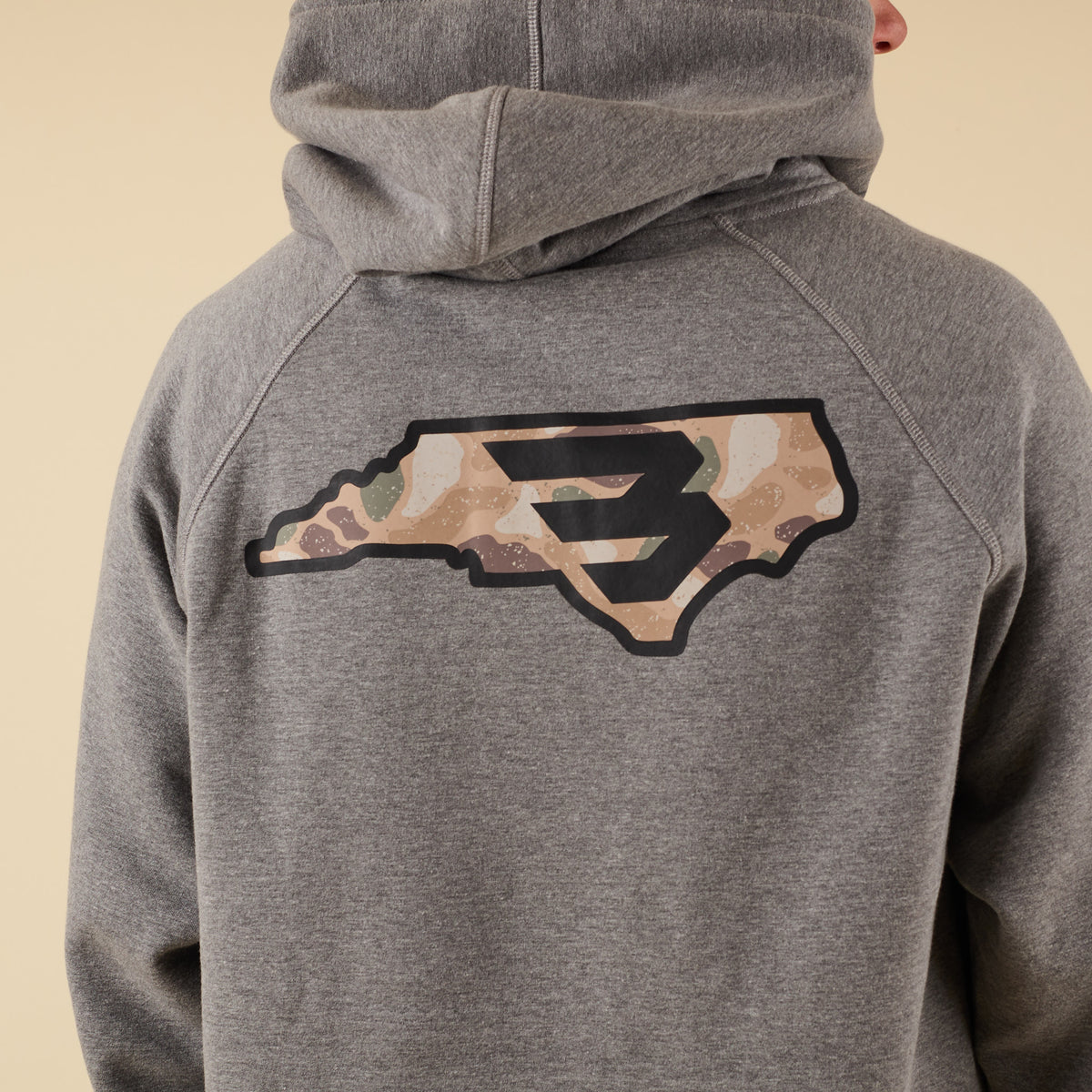 Close-up of the back of a gray hoodie showing a large camo-pattern logo graphic.