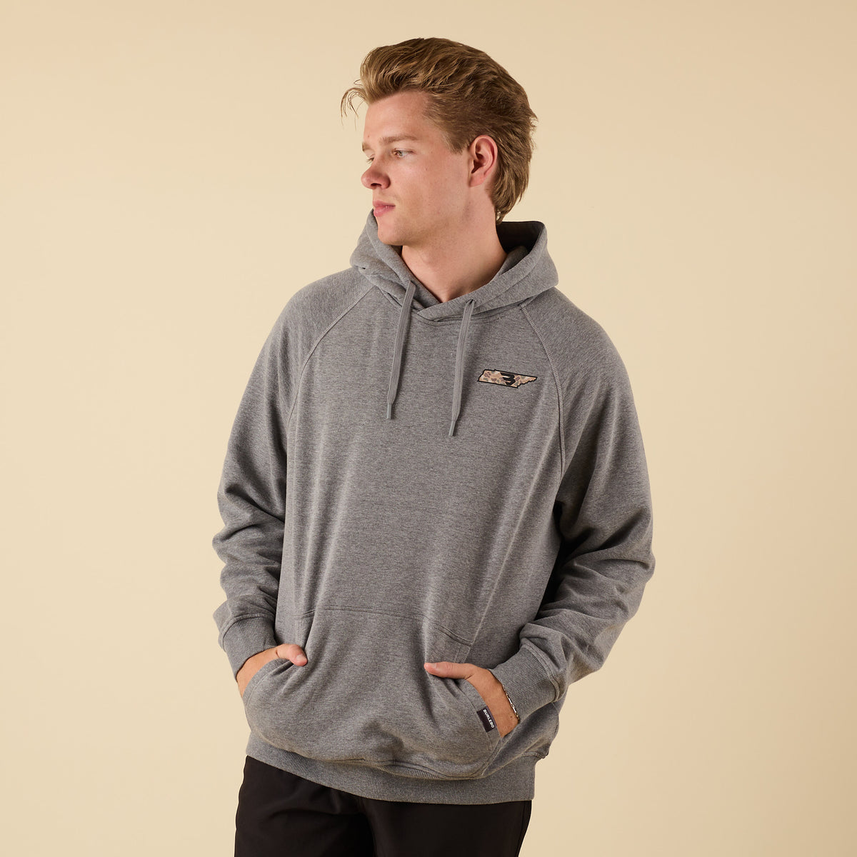 Front view of a man wearing a gray Burlebo hoodie with a small camo-pattern logo on the left chest, hands in front pocket.