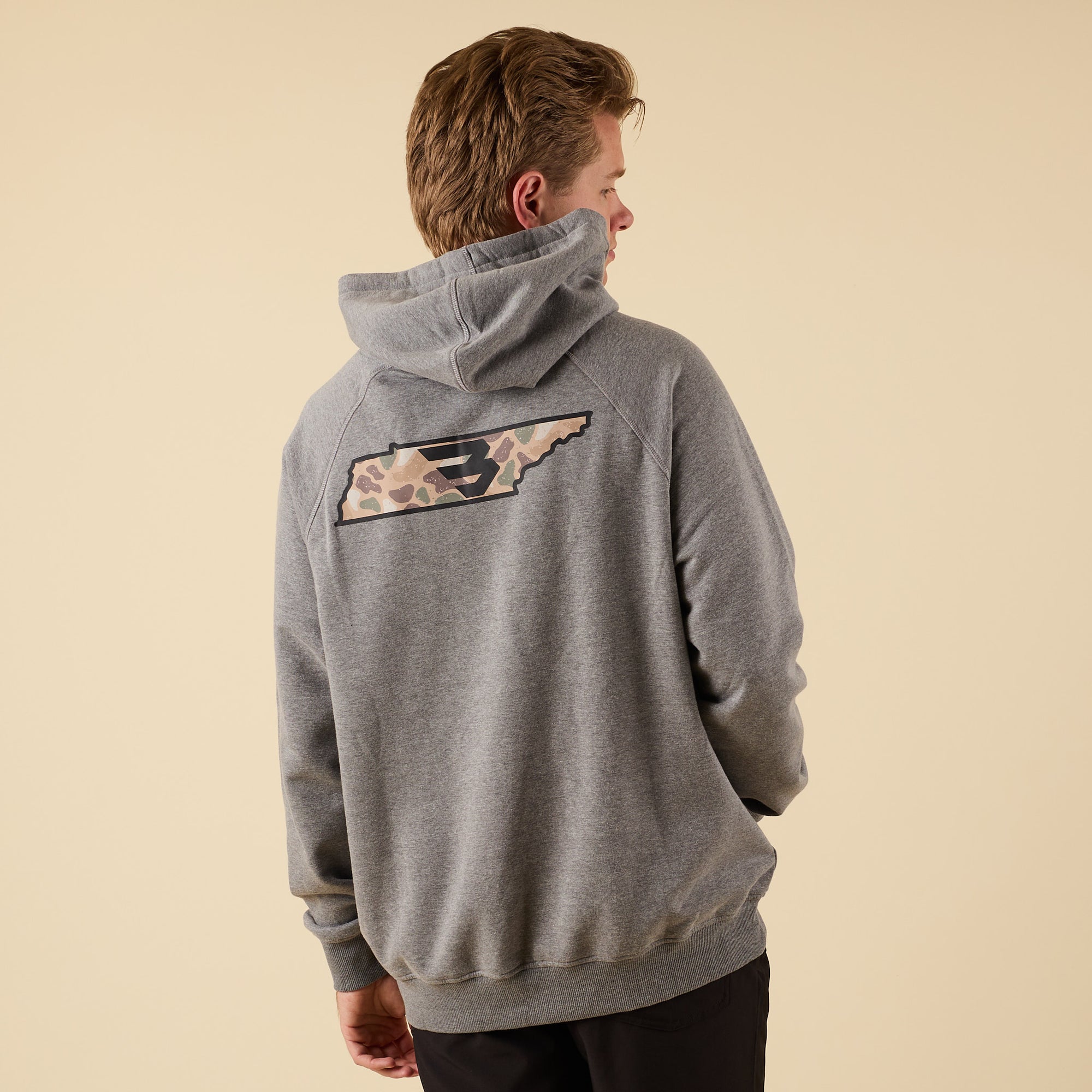 Rear angled view of a man in a gray Burlebo hoodie showing the large camo-pattern logo graphic on the back.