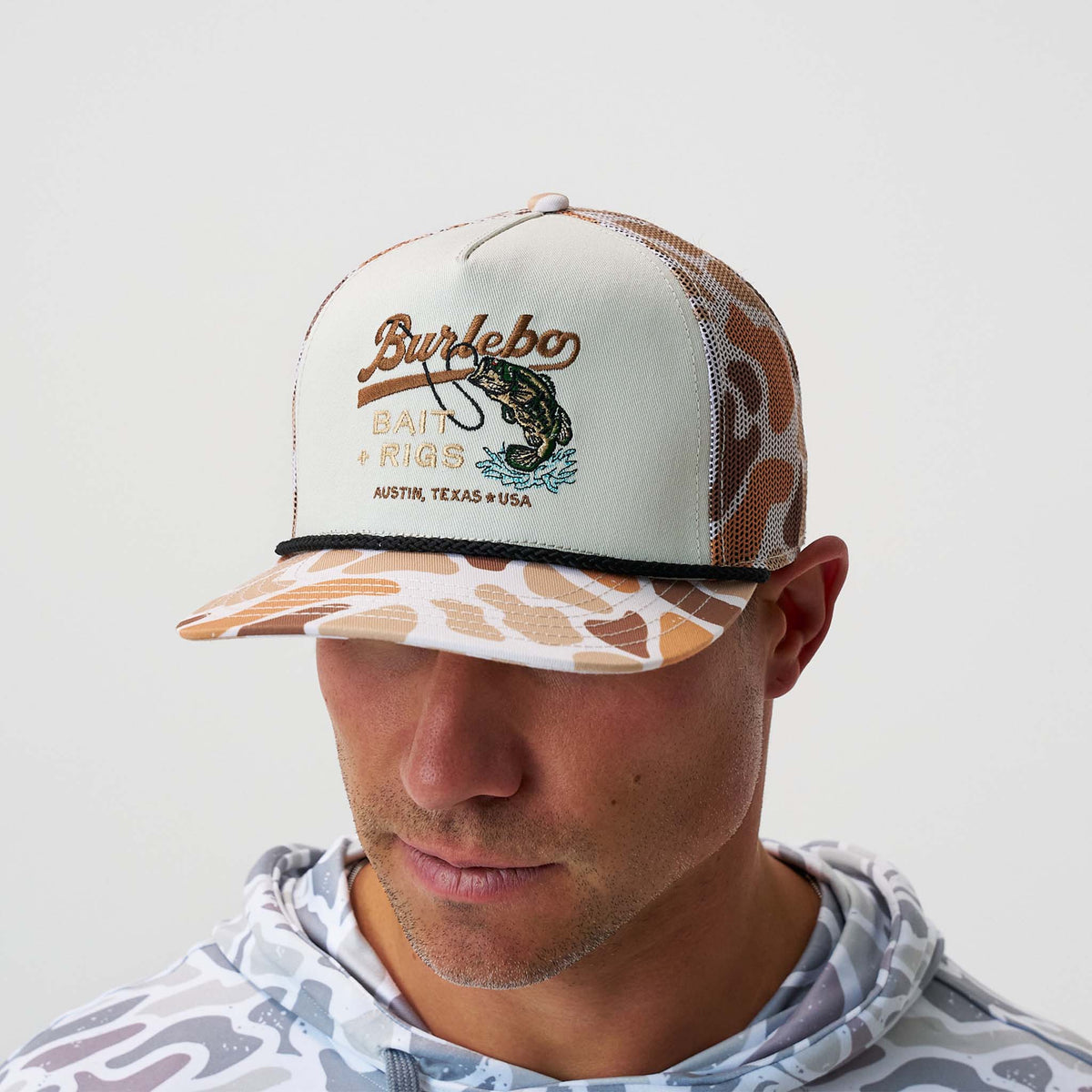 Person wearing a Burdeco cap with a camouflage pattern on a white background