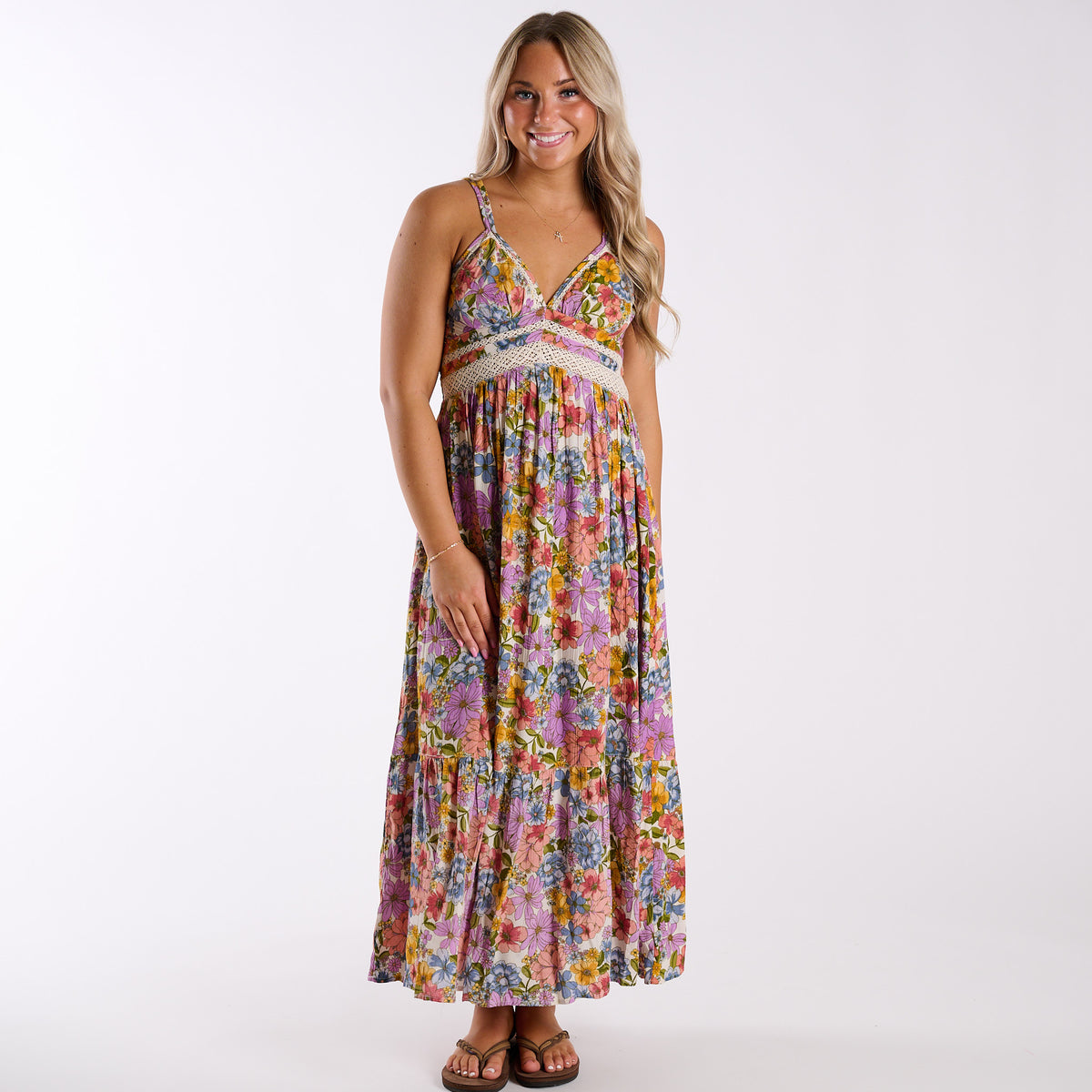 Woman wearing a colorful floral and lace inset sleeveless maxi dress on a white background