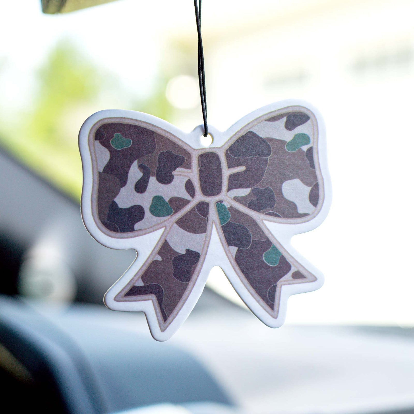Hanging bow-shaped air freshener with a green and brown camo pattern, suspended from a car mirror.