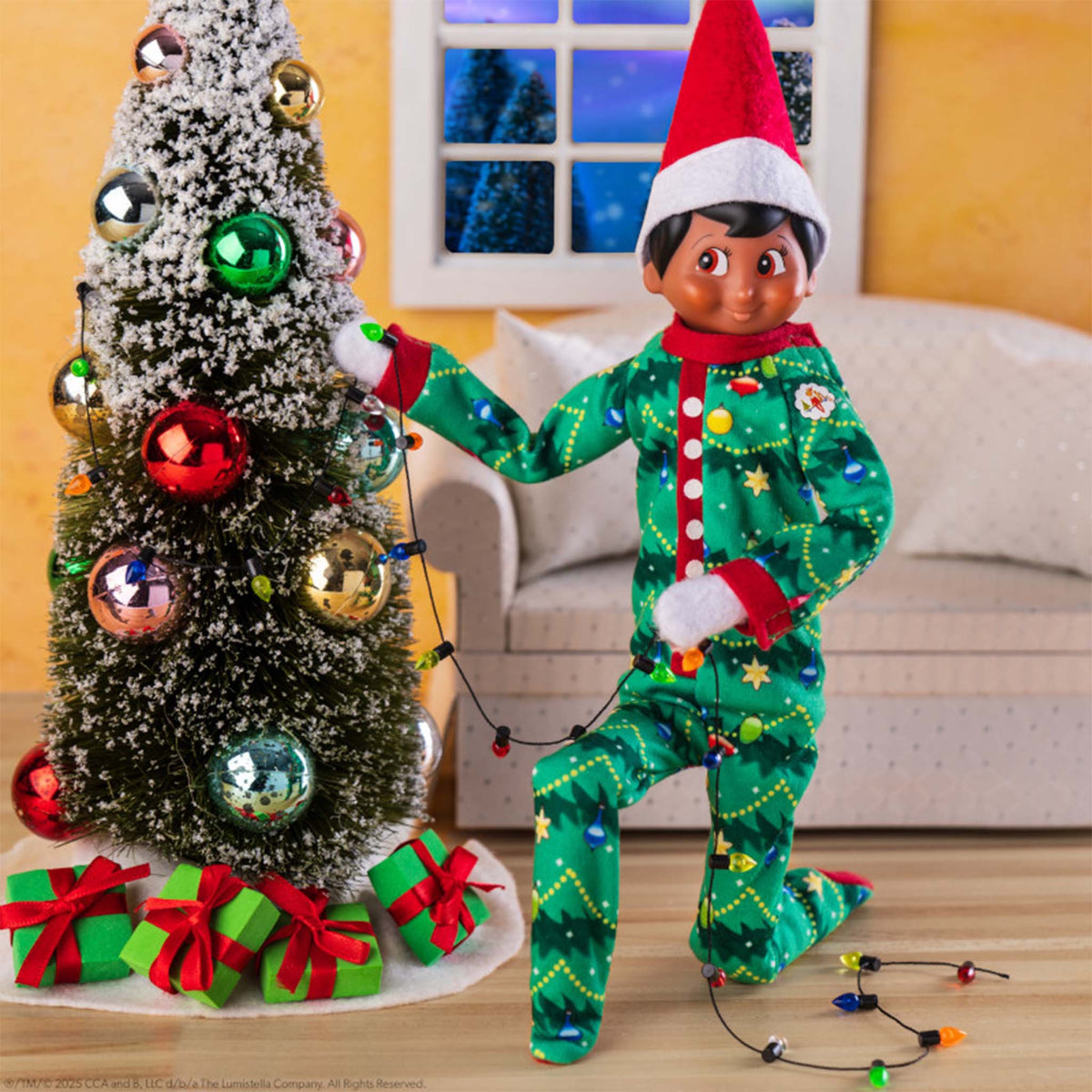 Elf on the Shelf in a green pajama set with a Christmas tree and decorations.