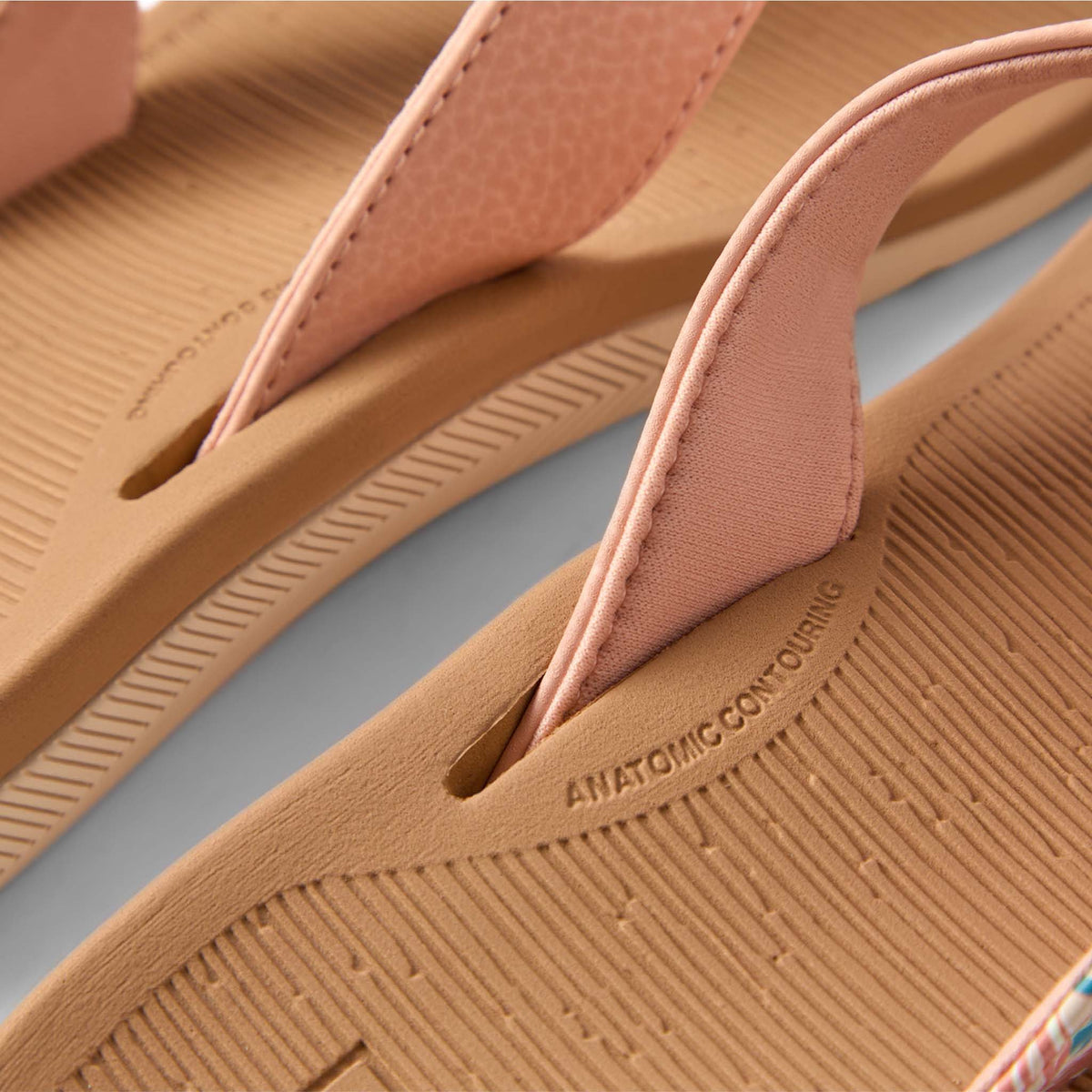 Close-up of tan sandals with pink straps on a light blue background