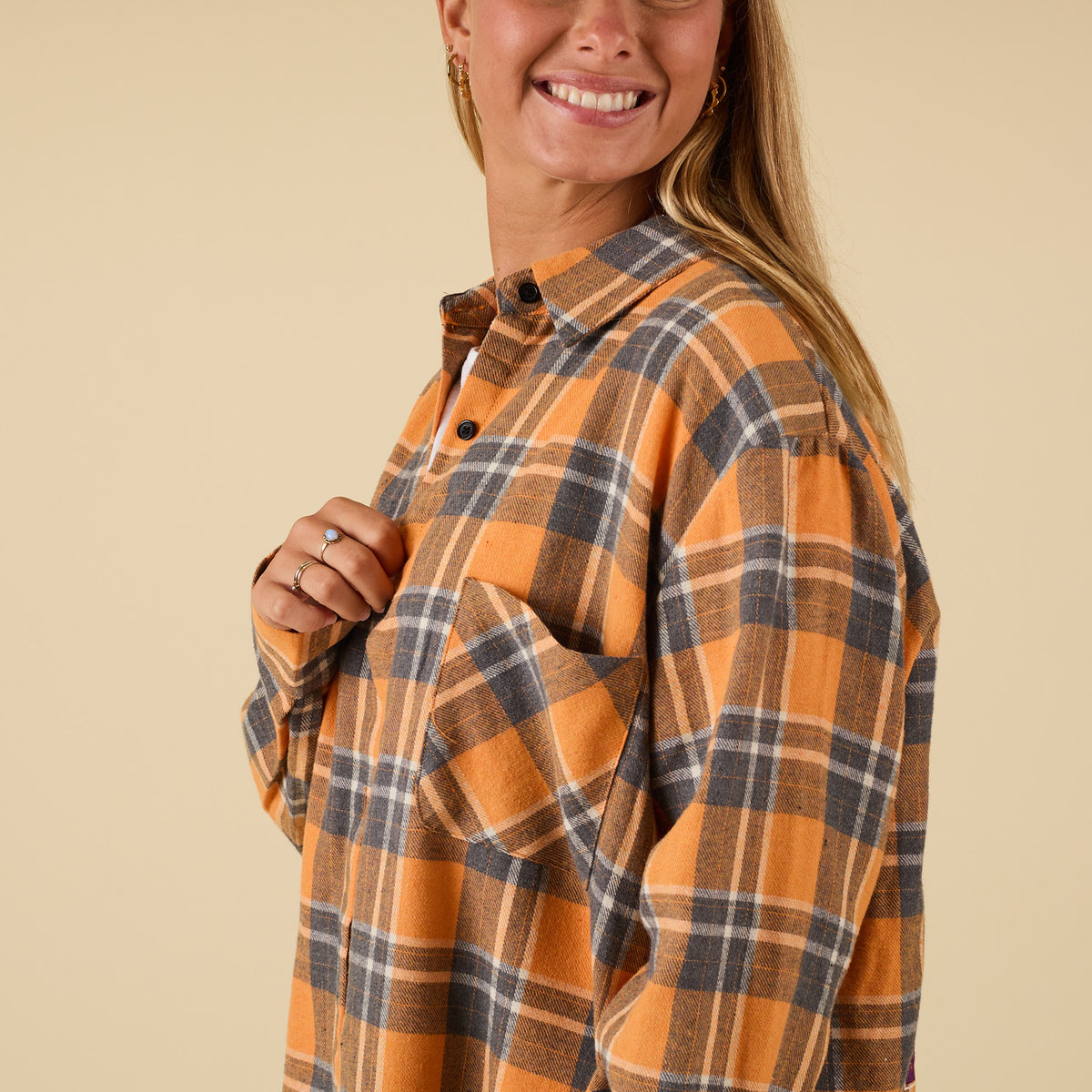 Woman wearing an orange and brown plaid shirt against a beige background