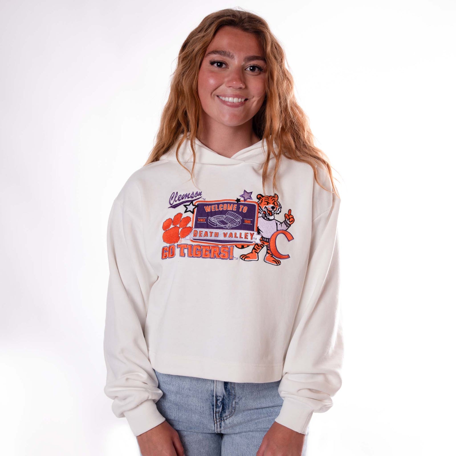 Front view of woman wearing white cropped Clemson hoodie with layered mascot patch design.