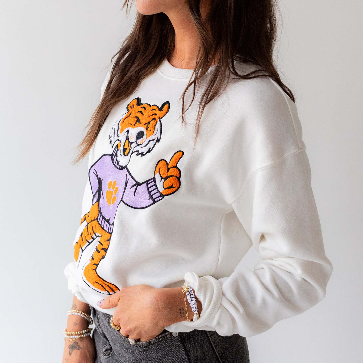 Side view of woman wearing white crewneck with large chenille tiger mascot patch.