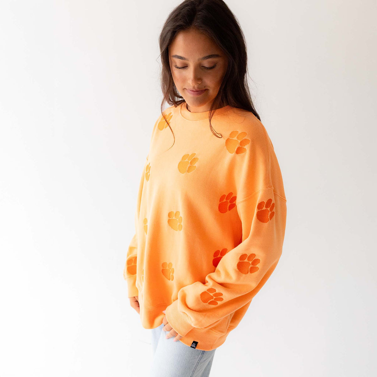 Side view of woman wearing sherbert orange crewneck with allover paw print design.