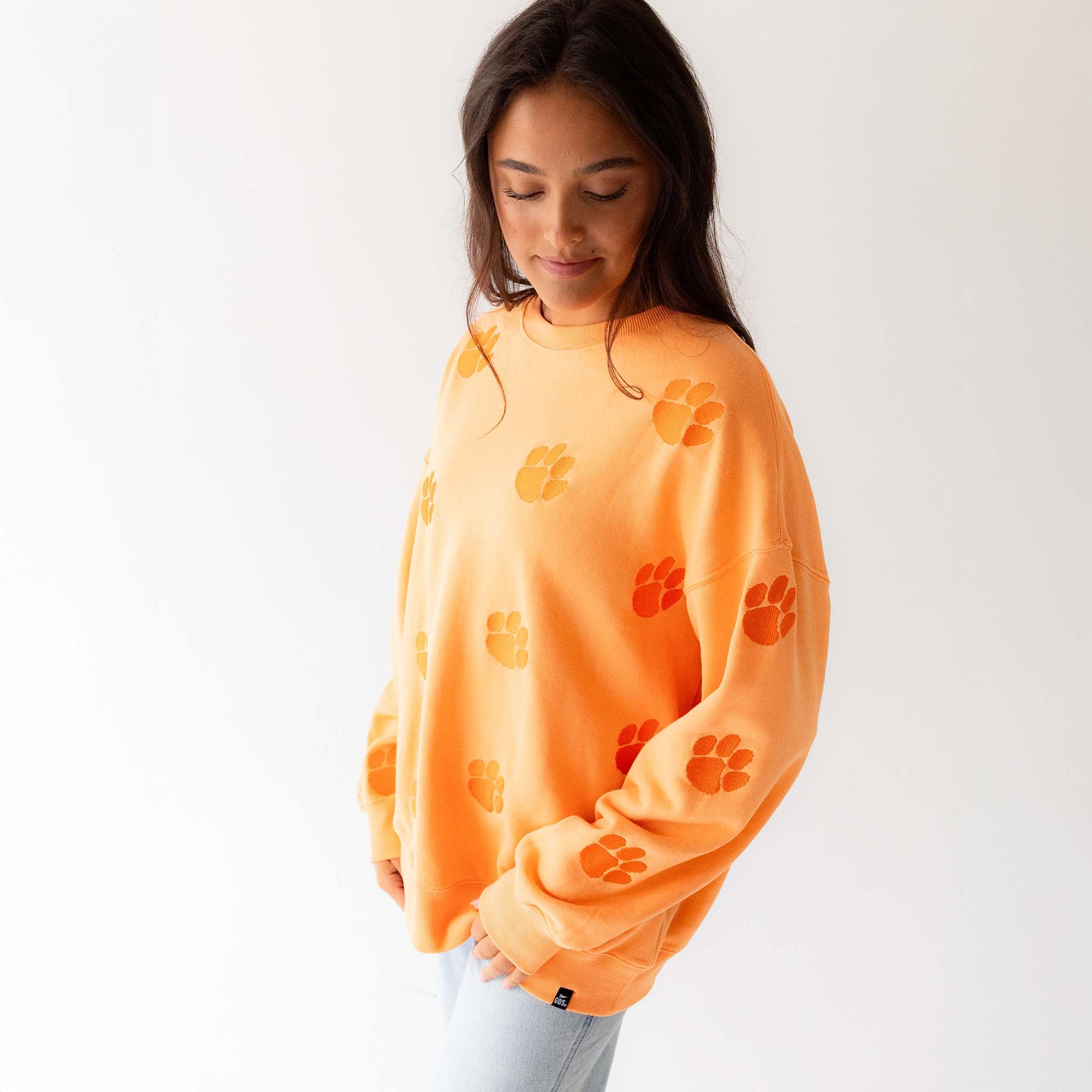 Side view of woman wearing sherbert orange crewneck with allover paw print design.