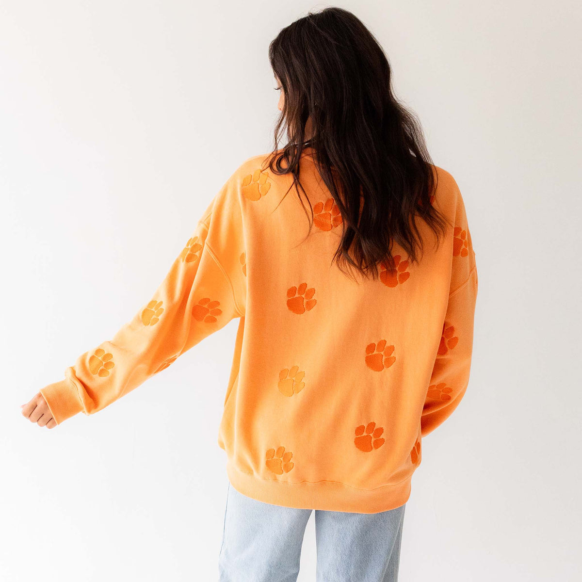 Back view of sherbert orange Clemson crewneck featuring repeating paw prints.