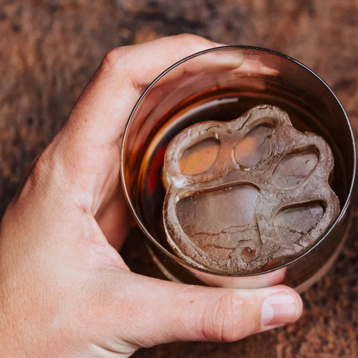 Hand holding a glass with a tiger paw-shaped Clemson University ice cube inside.