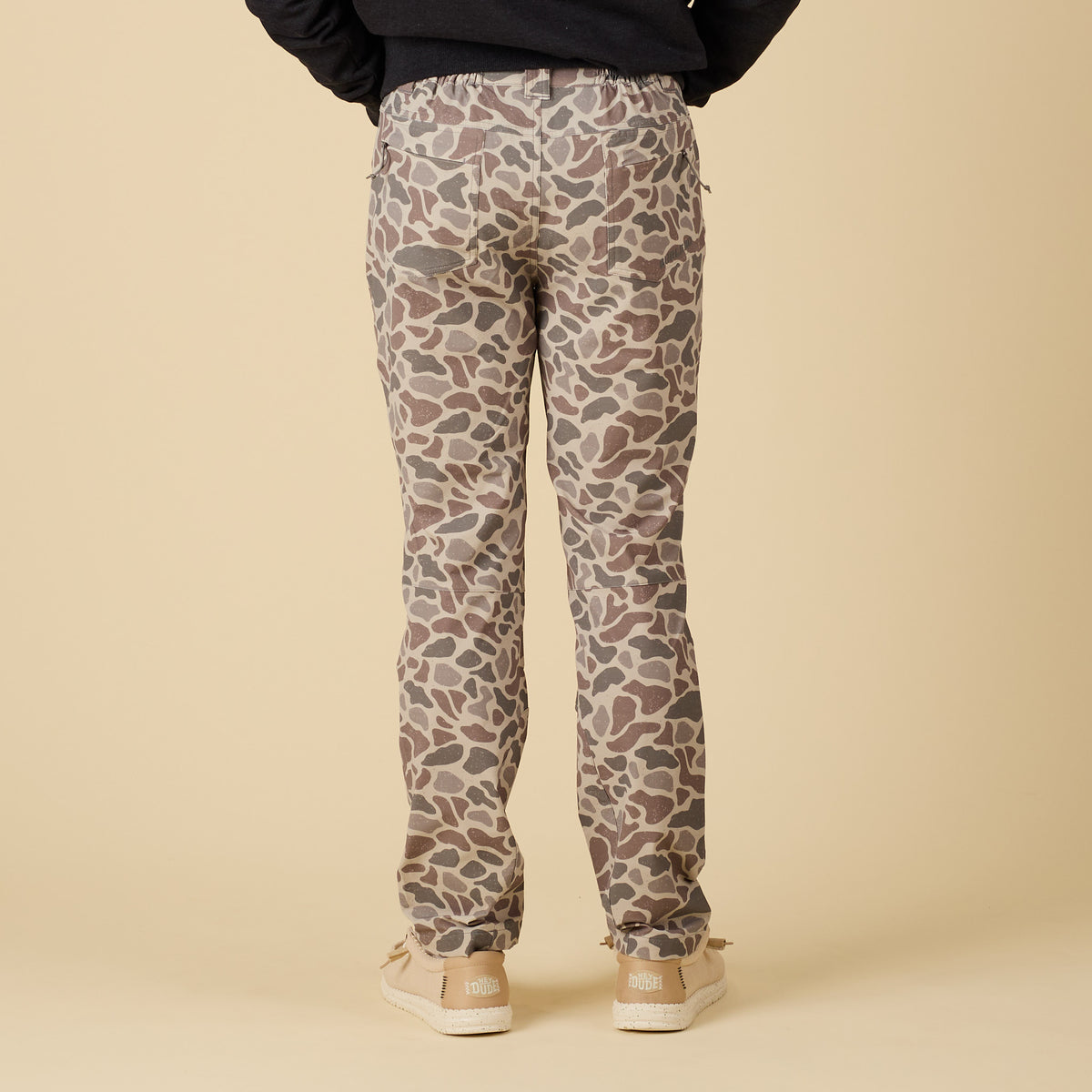 Back view of men’s pants in tan, brown, and gray deer camo print, shown with back pockets.