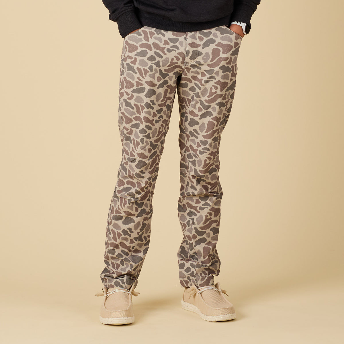 Full front view of men’s pants in tan, brown, and gray deer camo print, paired with casual shoes.