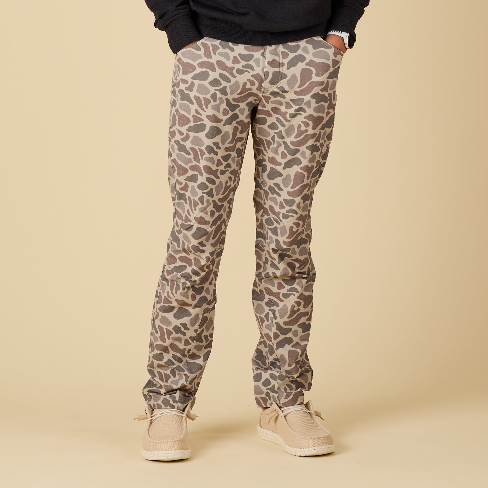 Full front view of men’s pants in tan, brown, and gray deer camo print, paired with casual shoes.