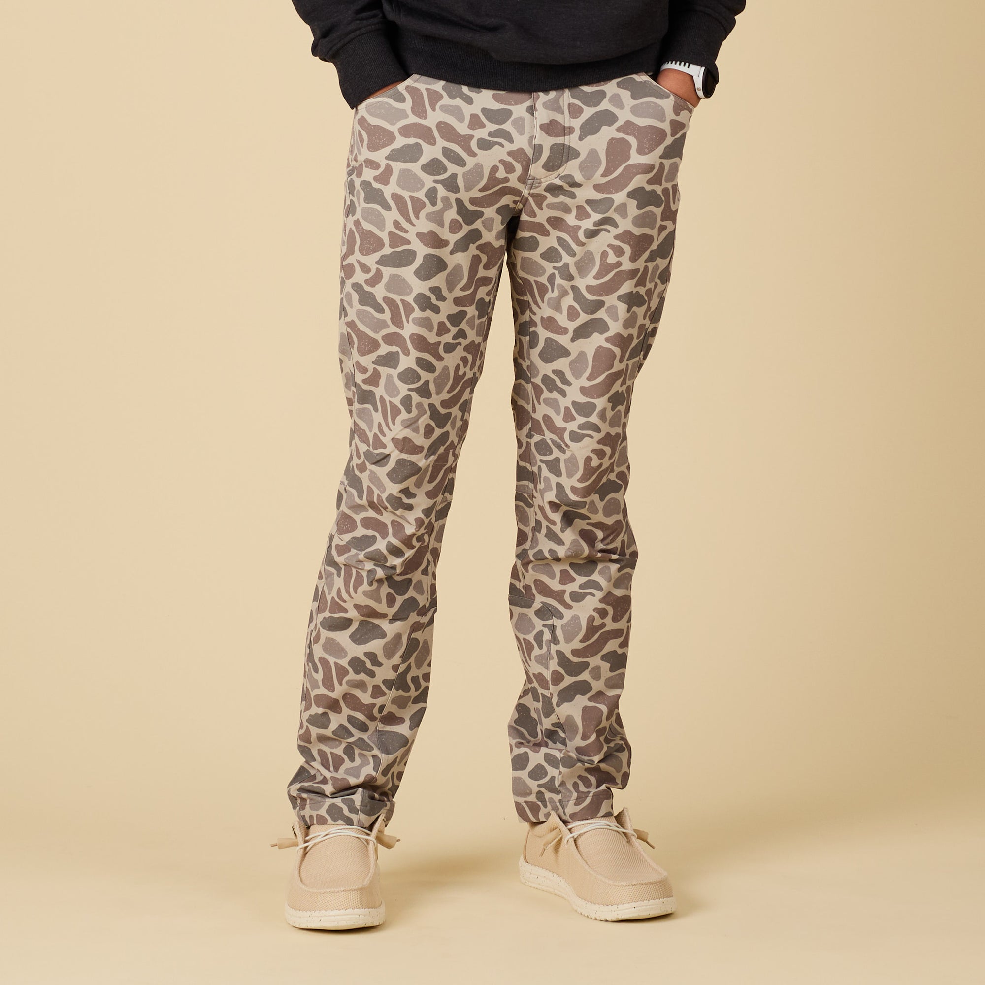Full front view of men’s pants in tan, brown, and gray deer camo print, paired with casual shoes.