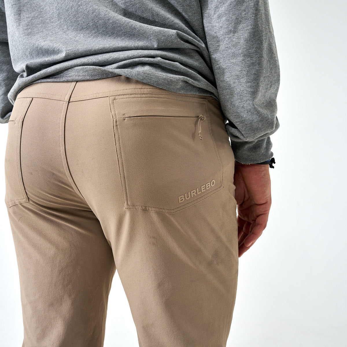 Back view of Burlebo Challenger Pants in cobblestone khaki with logo above pocket, styled with a gray long sleeve shirt.