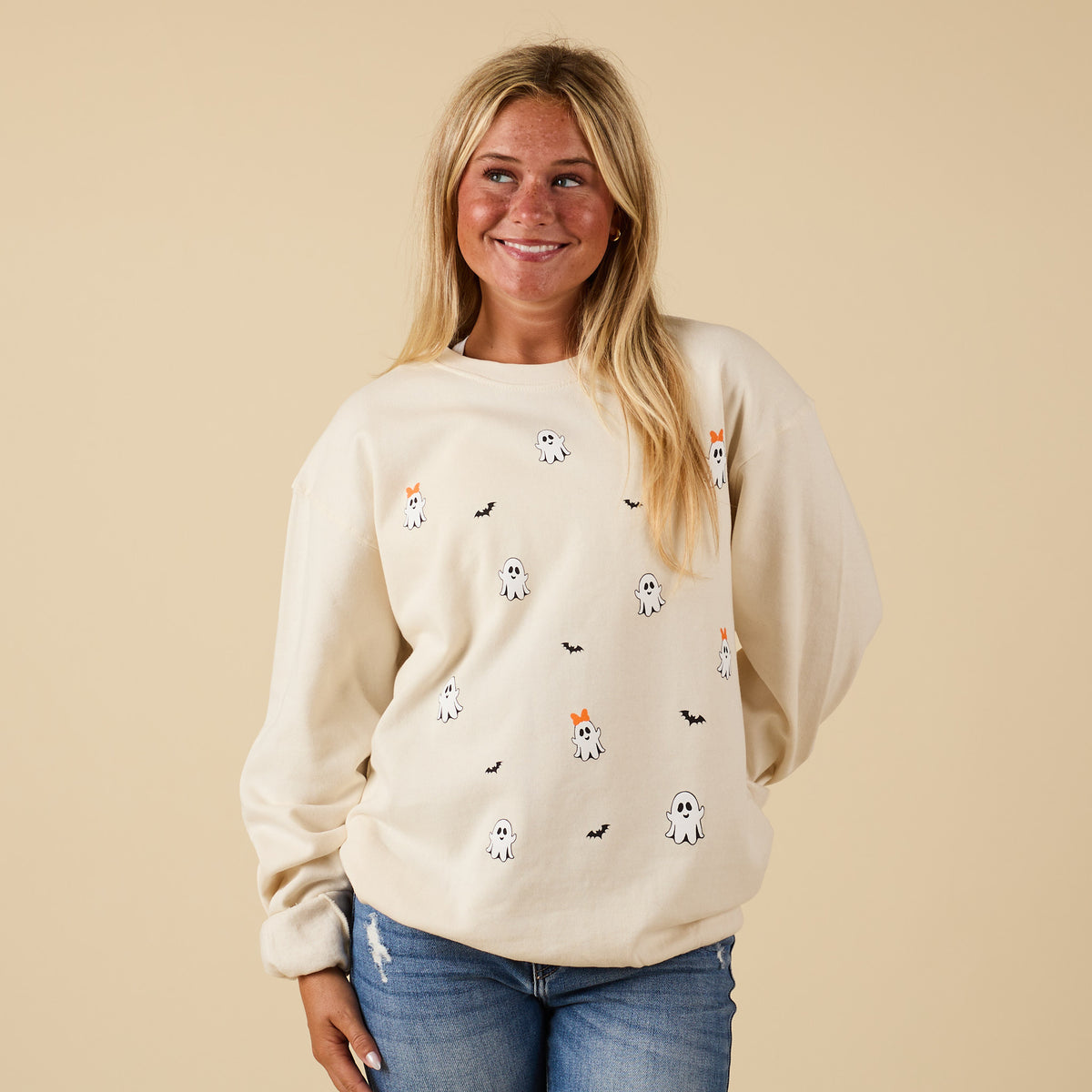 Sand crewneck sweatshirt with ghost and bat graphic print, shown on model from the front styled with jeans.