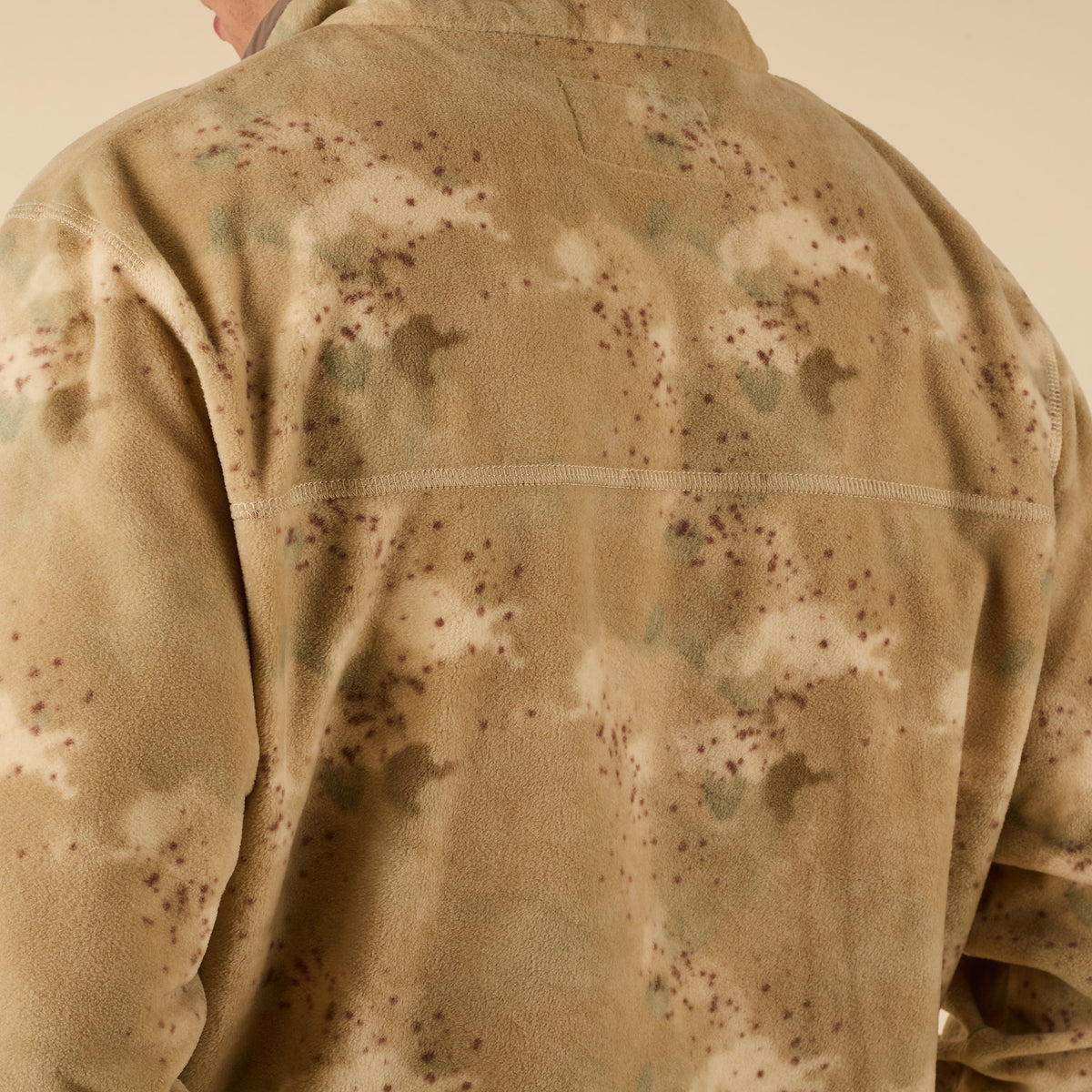 Close-up of back shoulder detail on tan camo fleece fabric with subtle green and brown pattern.