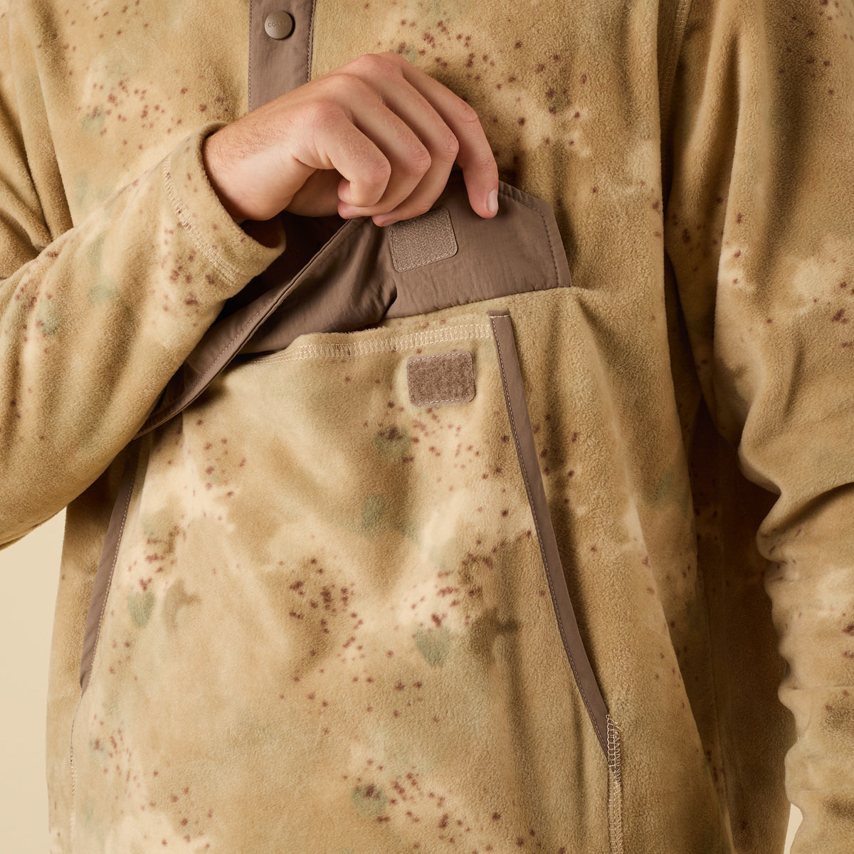 Close-up of a person wearing a beige camouflage jacket with a brown patch.