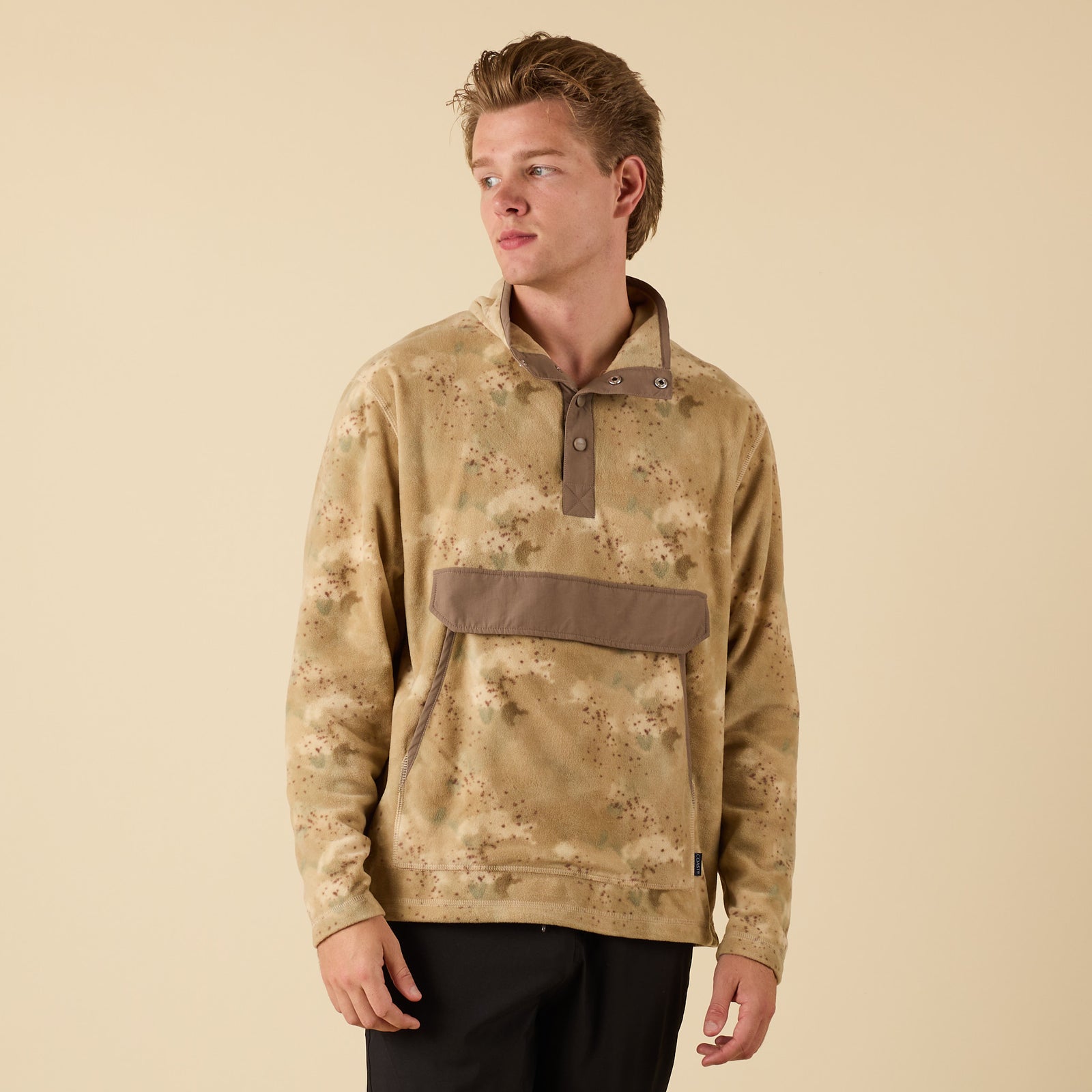 Person wearing a camouflage pullover with a pocket on a beige background
