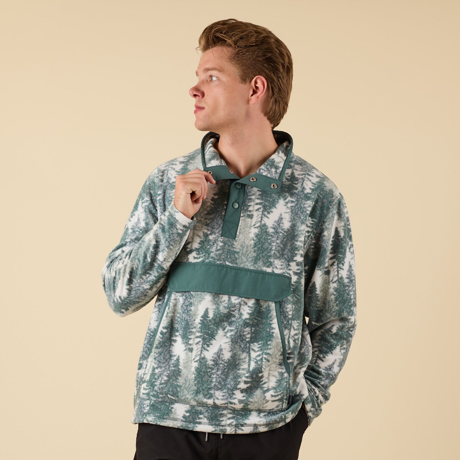 Front view of man wearing Crosby Fleece Quarter Snap Pullover in Spruce Trees print with snap collar and flap front pocket.