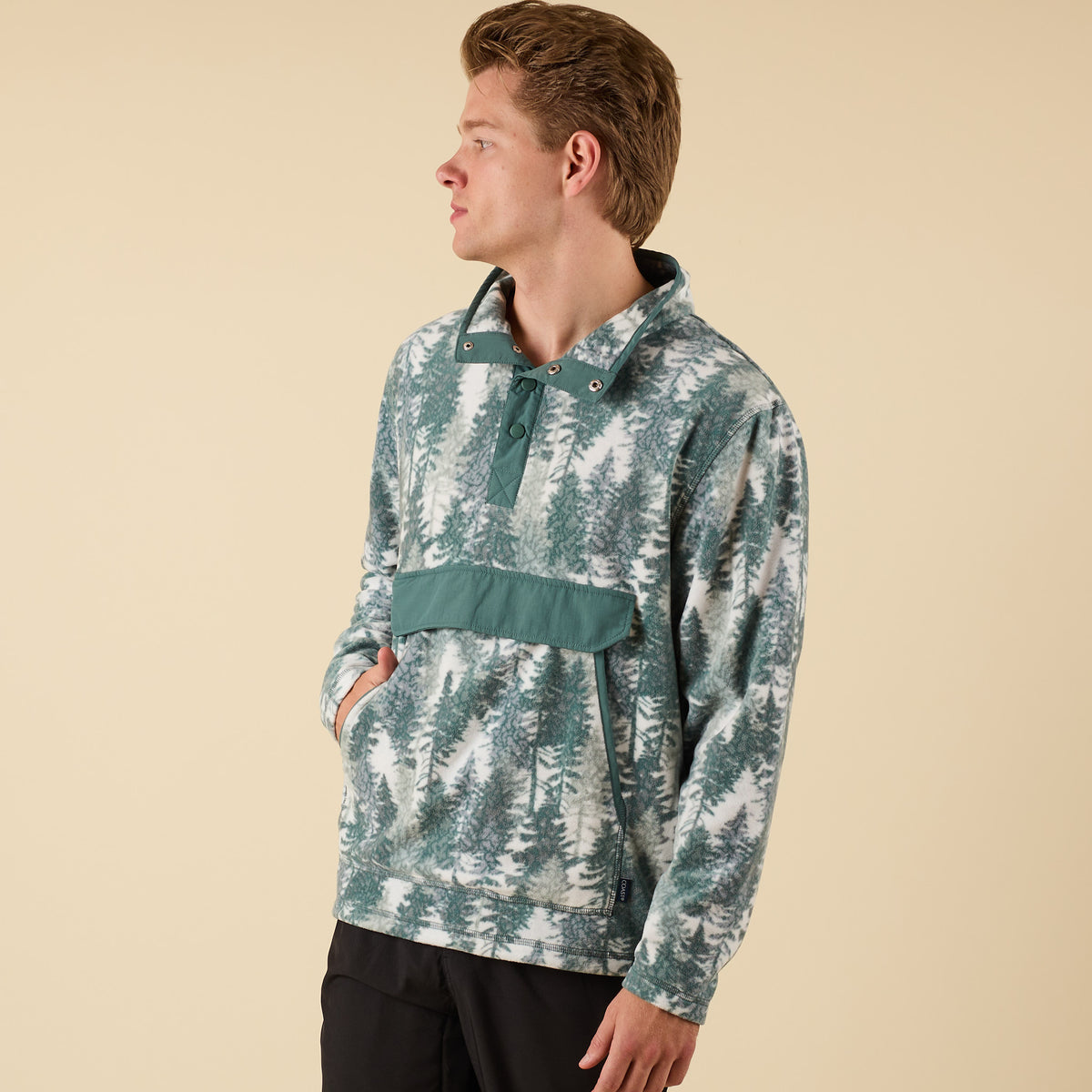 Side view of Crosby Fleece Quarter Snap Pullover in green and white spruce tree pattern with hands in front pocket.