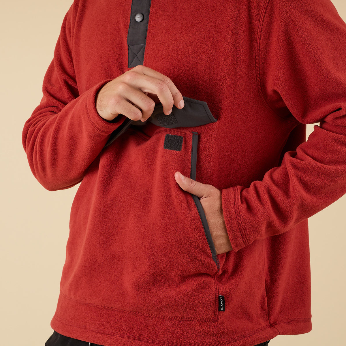 Close-up of front pocket on red fleece pullover showing Velcro flap and contrast trim.