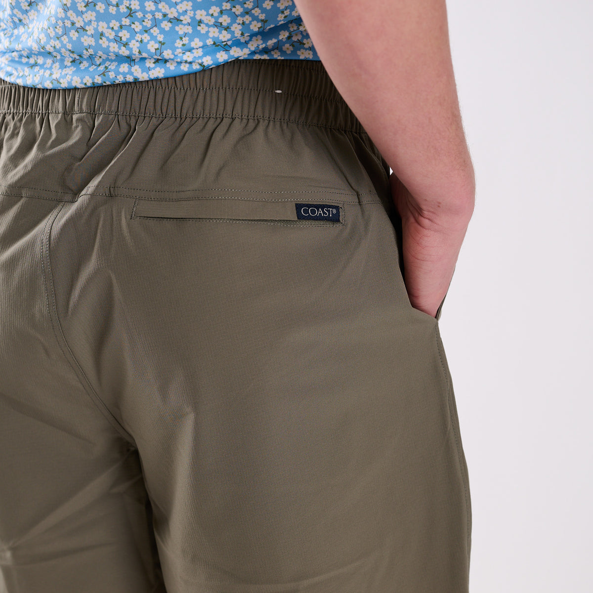 Person wearing olive green pants with a visible brand logo on a plain background