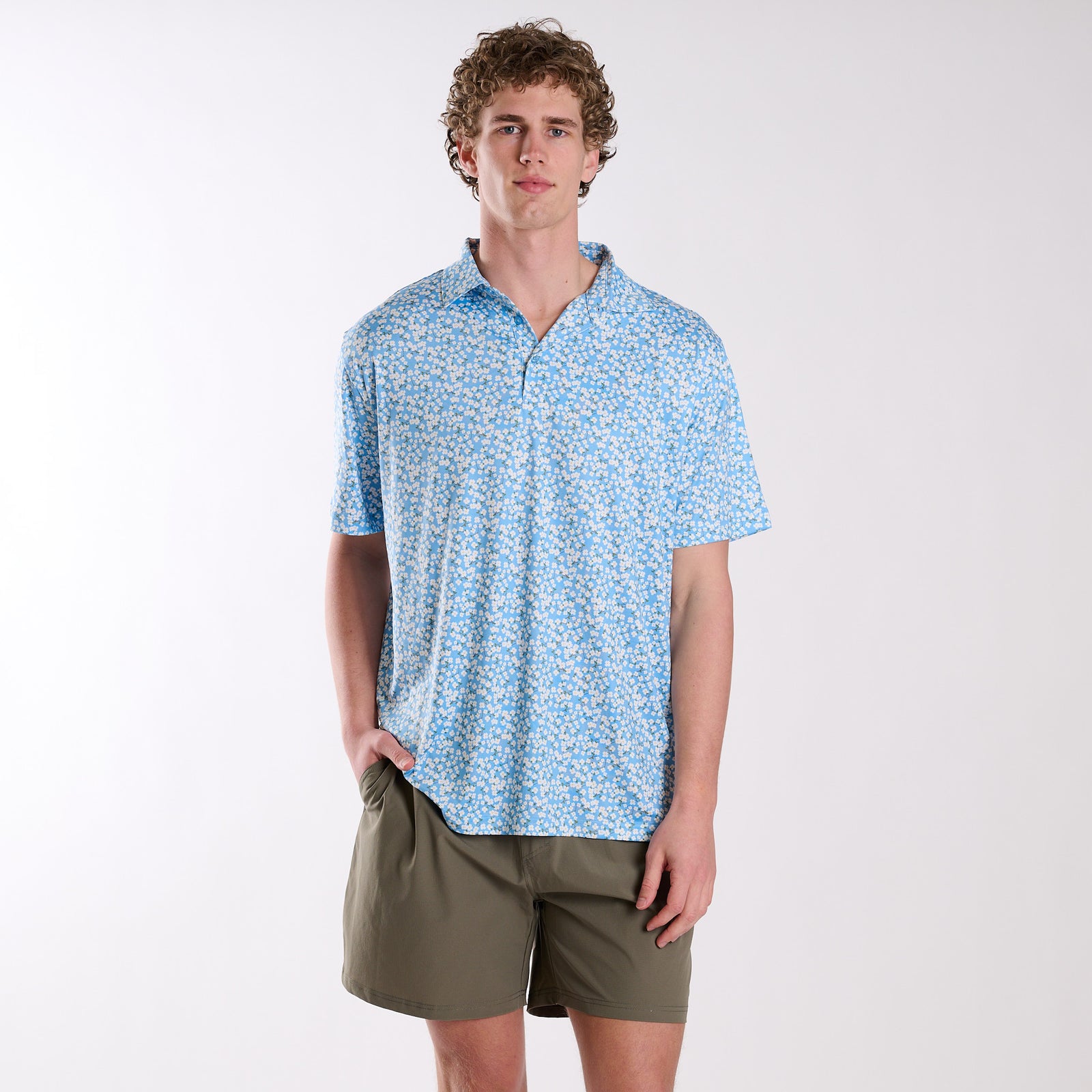 Man wearing a blue patterned shirt and green shorts on a white background