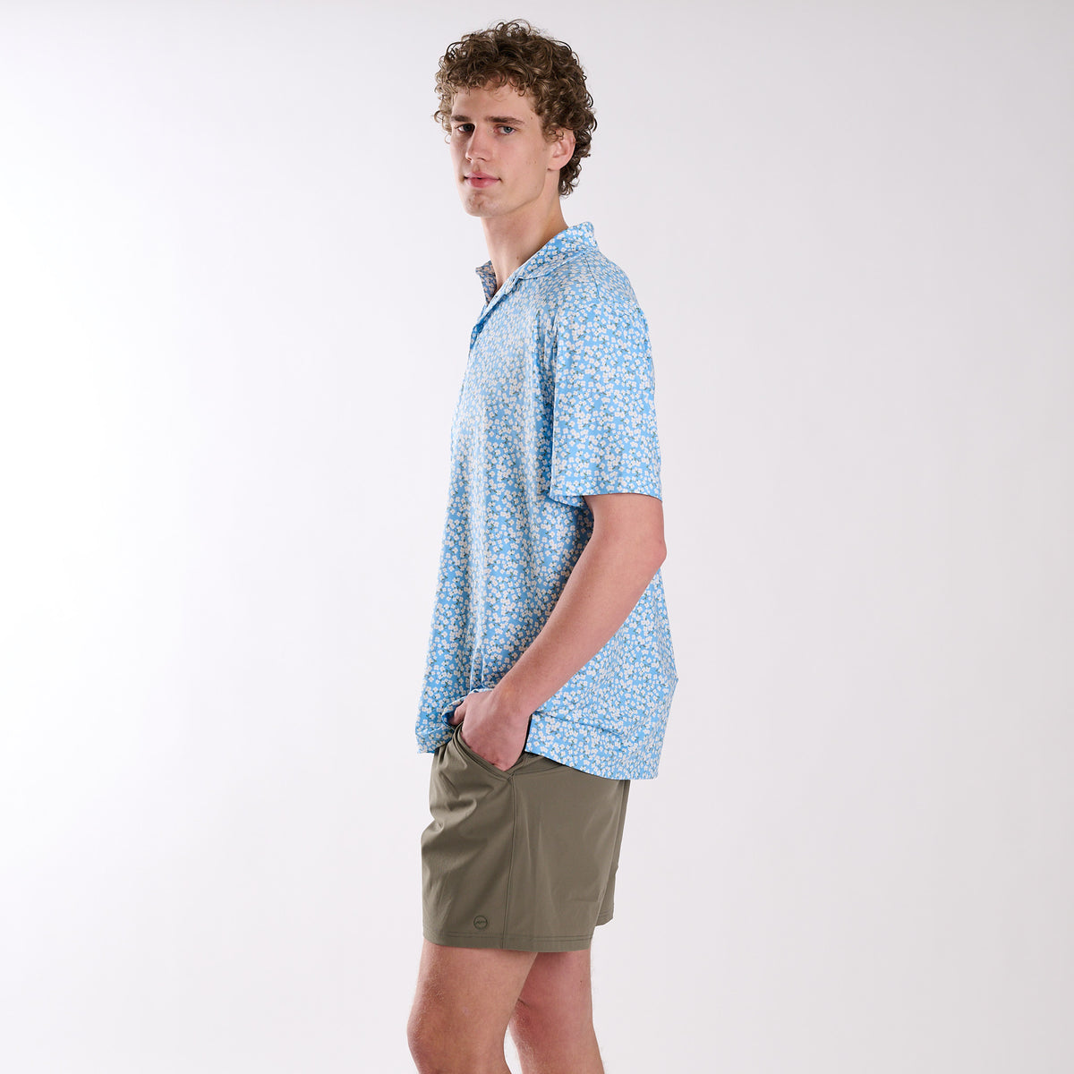 Man wearing a light blue patterned shirt and green shorts on a white background