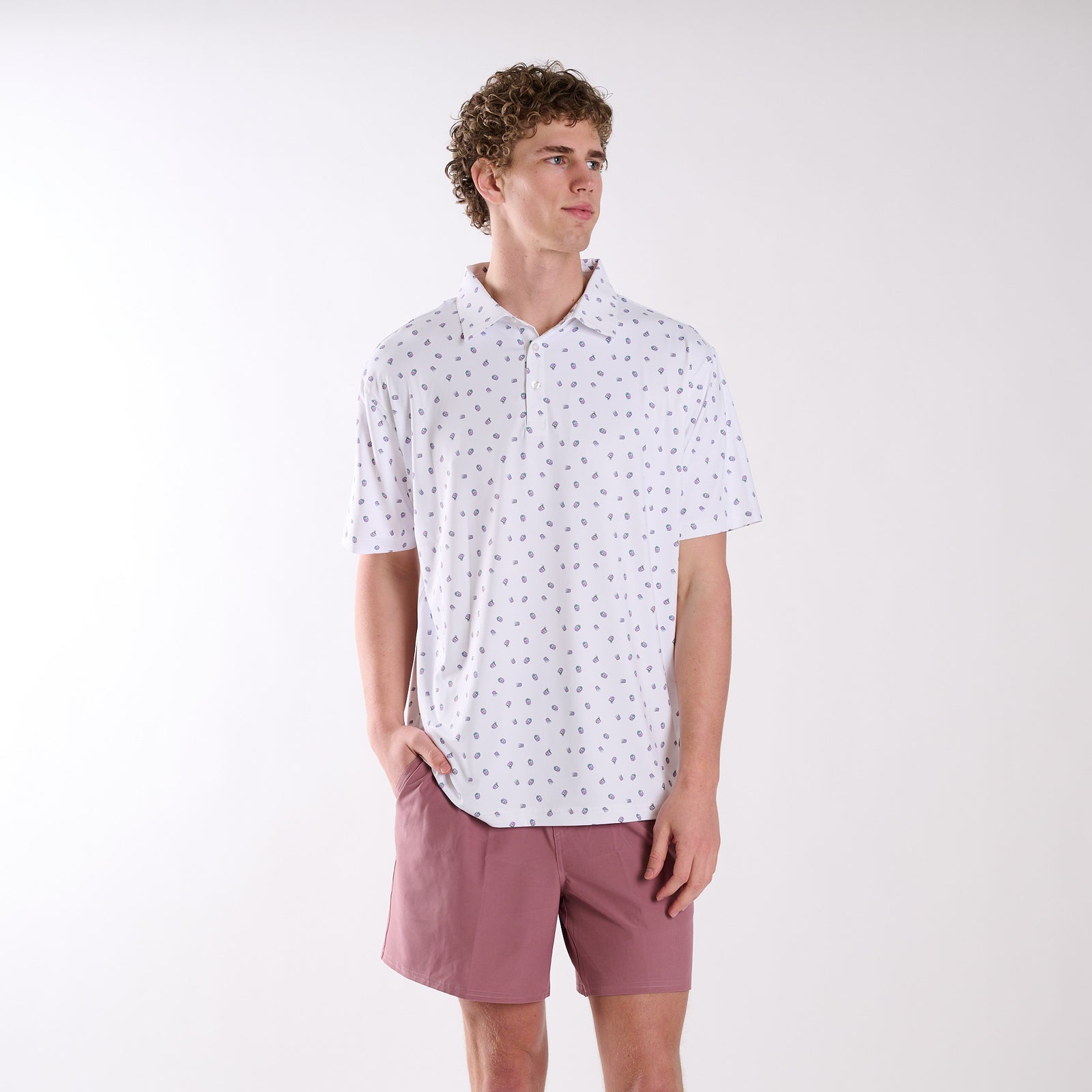 Full front view of COAST Transfusion Icon Printed Polo in white with transfusion icon print, worn by a model with pink shorts in a studio setting.