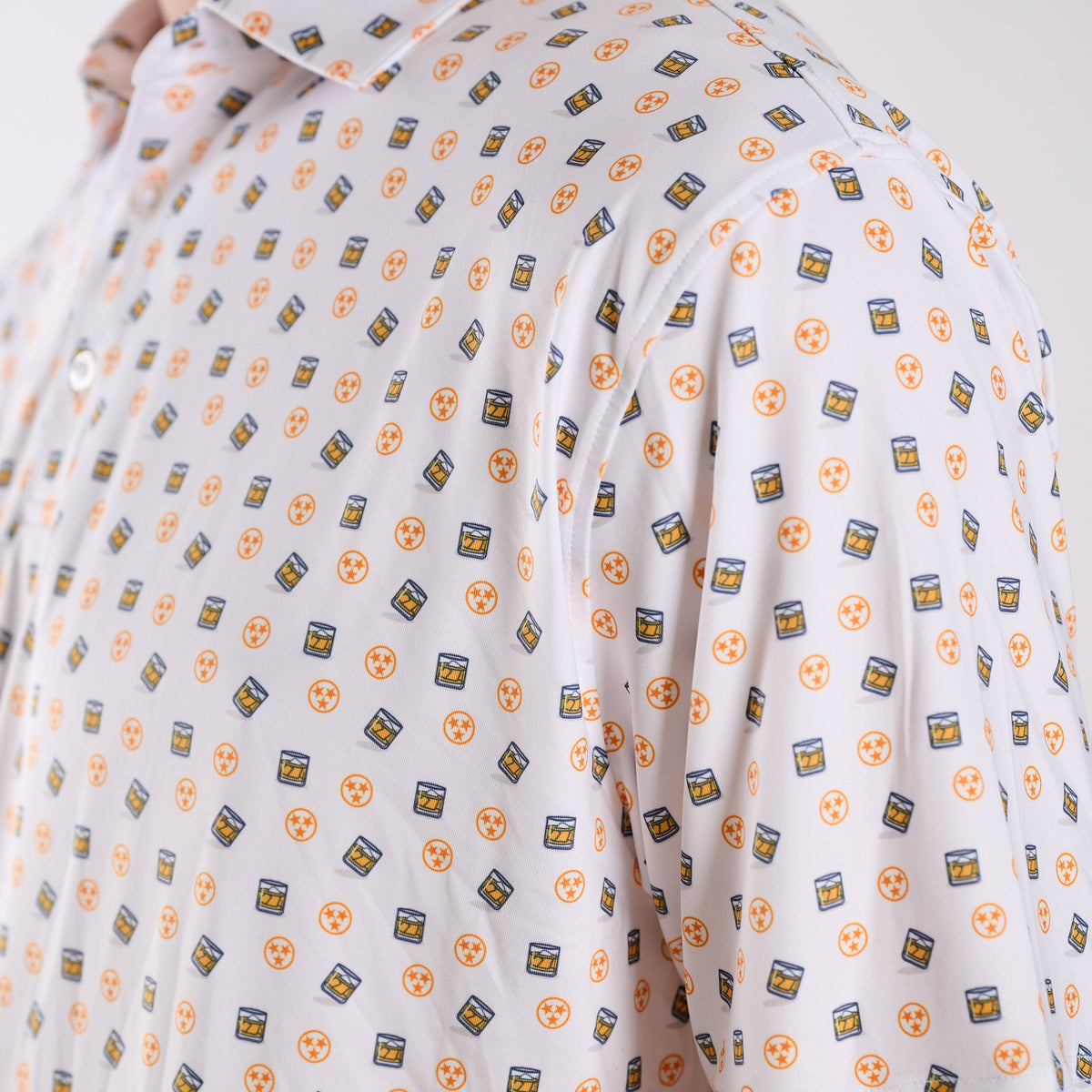 Detailed fabric view of COAST Tennessee Whiskey Tri Star Printed Polo in white with repeating whiskey glass and Tennessee tri-star icons across the material.