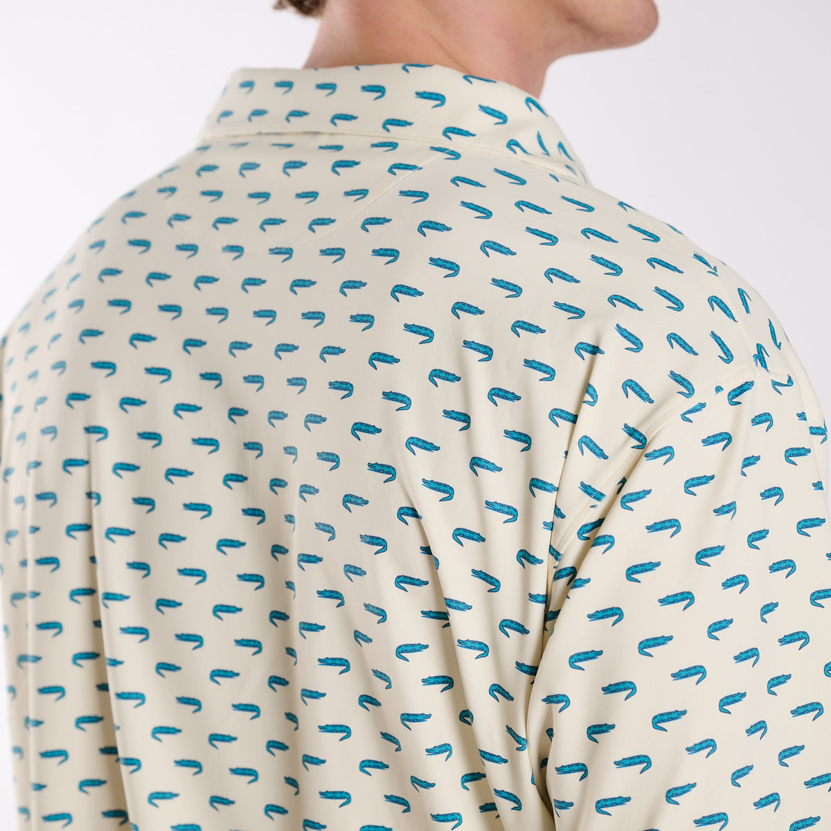 Back shoulder detail of COAST Florida Gator Printed Polo in light yellow showing the repeating teal alligator pattern across the fabric.