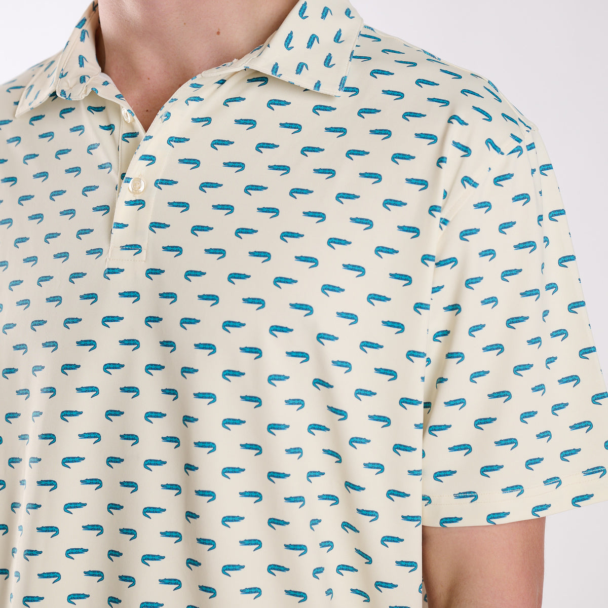 Close-up of COAST Florida Gator Printed Polo in light yellow featuring repeating teal alligator icons with a classic collar and button placket.