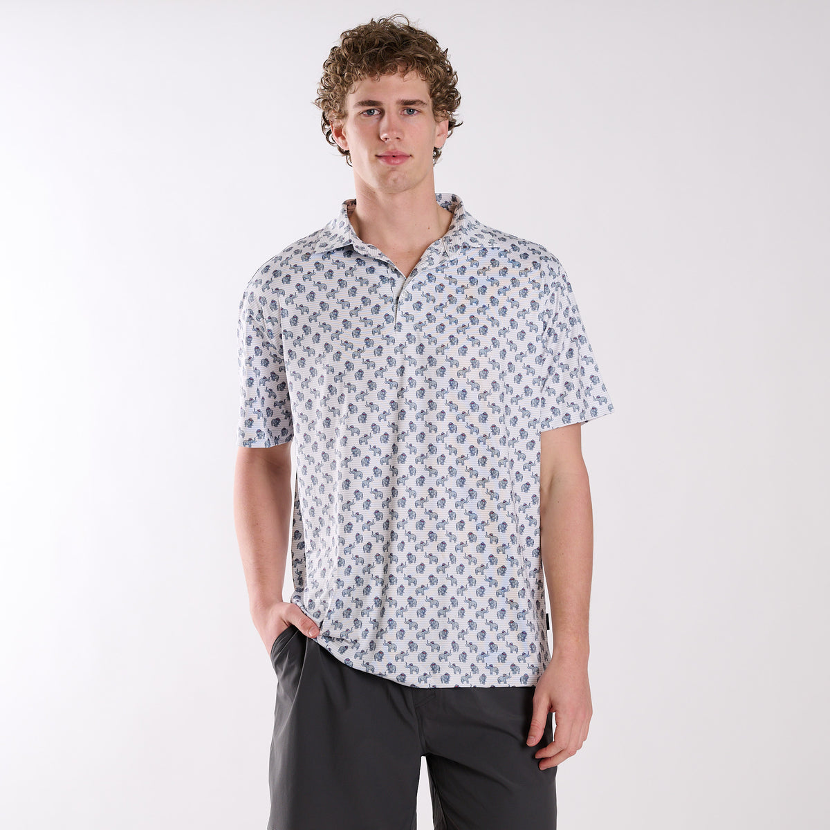 COAST Alabama Elephant Printed Polo in white with repeating elephant and red cap pattern, worn by a model with dark shorts against a light studio background.
