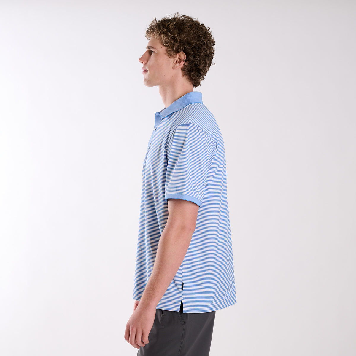 Side profile of model wearing COAST Stripe Performance Polo showing short sleeves and micro-stripe fabric pattern.
