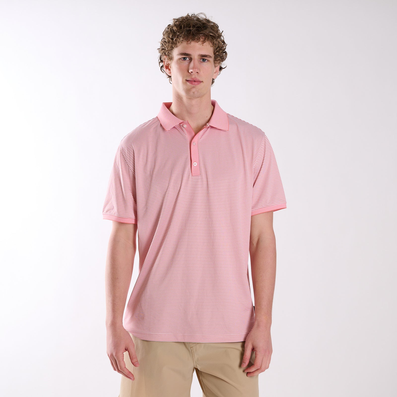 Front view of COAST micro-stripe performance polo in terracotta and white, worn by a model with khaki shorts against a neutral studio background.