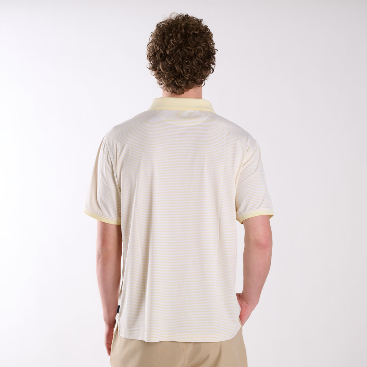 Back view of COAST micro-stripe performance polo in pale yellow with white stripes, shown on a model in a studio setting.