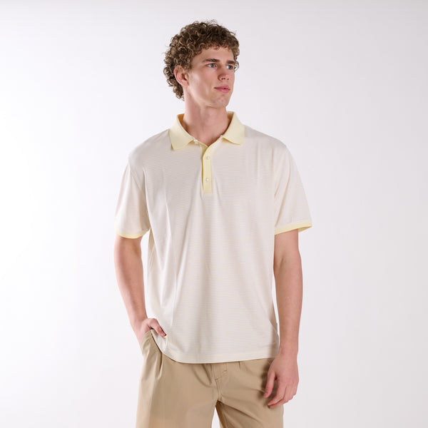 Front view of COAST micro-stripe performance polo in pale yellow with white stripes, worn by a model with one hand in pocket.