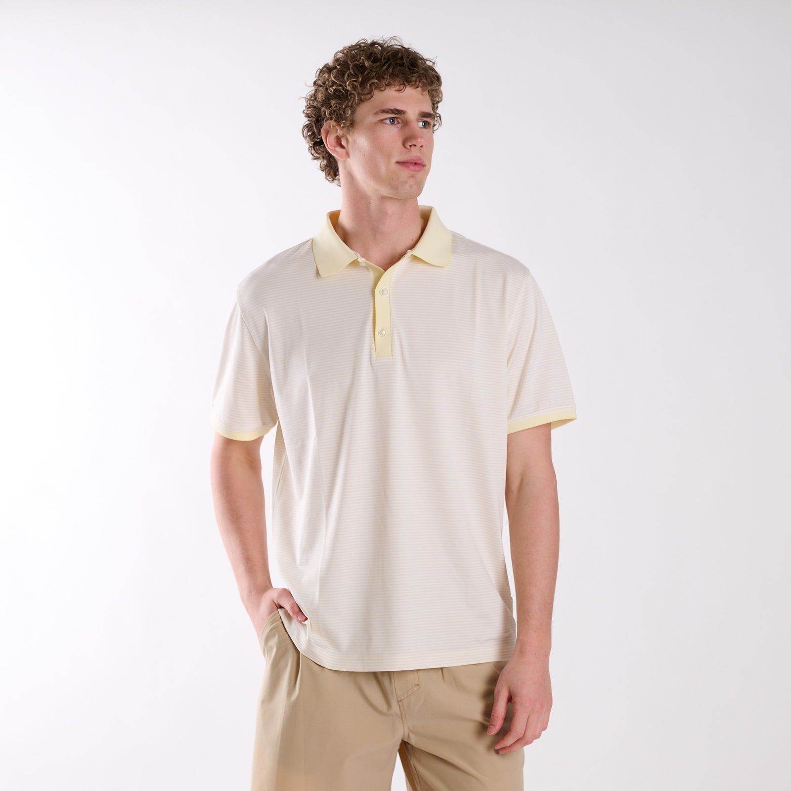 Front view of COAST micro-stripe performance polo in pale yellow with white stripes, worn by a model with one hand in pocket.